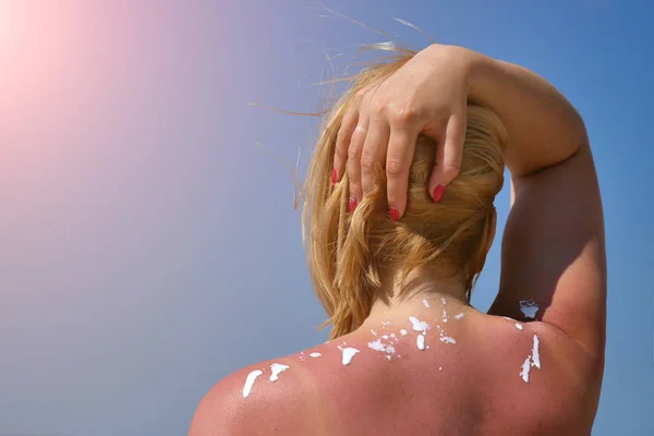 Frau reibt Sonnencreme auf seine Schulter. vor dem Hintergrund des Meeres. — Stockfoto