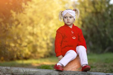 Küçük kız sonbahar bahçesinde bir balkabağının üzerinde otururken üzgün.