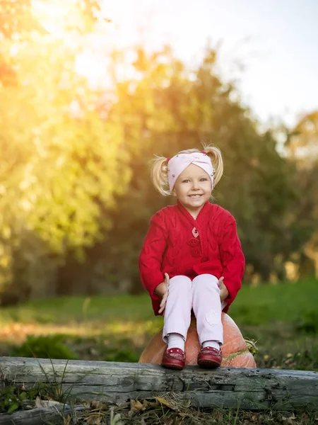 Petite fille assise sur une citrouille dans le jardin d'automne — Photo