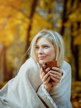Güz parkında, elinde bir fincan çayla ekoseye sarılmış güzel bir kız.