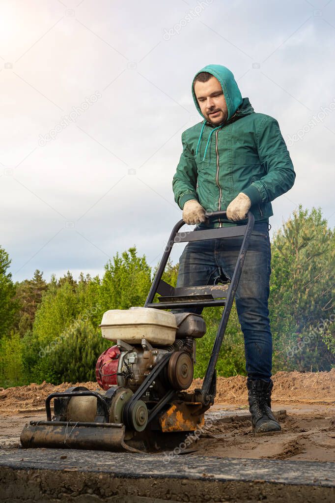a worker with a vibrating tamping machine rams the ground