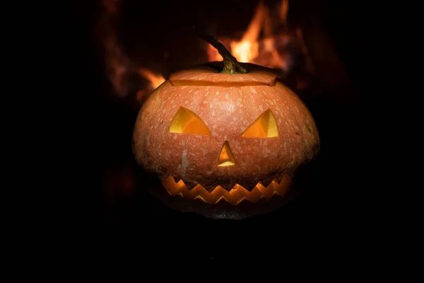 Creepy halloween pumpkin near a fireplace. Fire on the background.