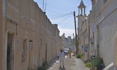 Pakistanlı adam eski bir asfaltsız sokak ve cami üzerinde yürüyor 