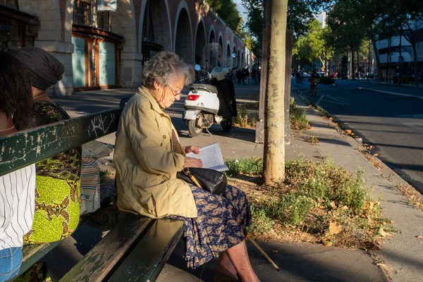 在巴黎的公共长椅上看书的老太太 — 图库照片