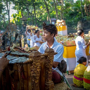 Ubud, Bali, Endonezya - 5 Mayıs 2018: Arka planda devam eden bir törenle geleneksel kıyafetler giyen geleneksel müzik aleti çalan genç bir müzisyen