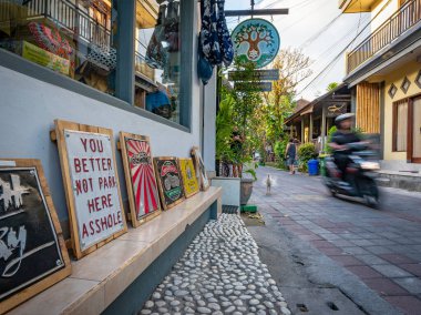 Hareketli sokak sahnesi bulanık tavuk ve motosikletçiler ve komik tabelalar, Ubud, Bali, Endonezya
