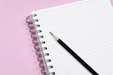 Çalışma alanı: Not defteri ve pembe bir arka plan üzerinde siyah kalem. Minimalist kompozisyon.