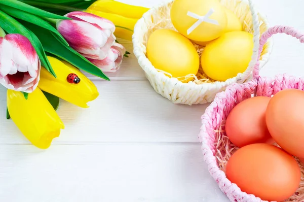 Pink and white baskets of colorful Easter eggs and a bouquet of tulips. White wooden background. Easter holiday concept.