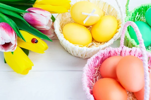 Baskets of colorful Easter eggs and a bouquet of tulips. White wooden background. Easter holiday concept.