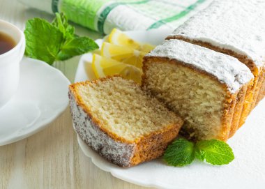 Pudra şekeri, bir yukarı bir beyaz tahta tabloda çay ve limon dilimleri ile servis ile bisküvi pasta dilimleri.