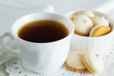 Bir fincan çay beyaz ahşap bir masa üzerinde küçük kurabiye ile.