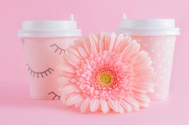 Kahve take-away ve pembe pastel arka plan üzerinde gerbera çiçek bardak. Kahve zamanı. Kopyalama alanı ile.