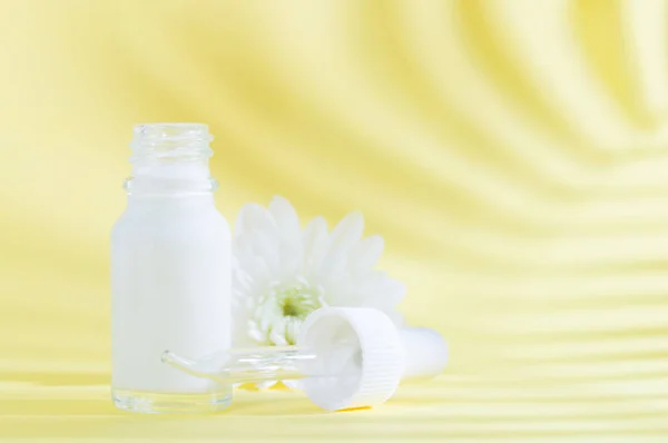 Natural cosmetics: serum with dropper and white flower on yellow background with shadow.
