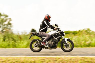 Genç adam yolda motosiklet sürüyor.