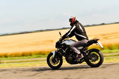 Genç adam yolda motosiklet sürüyor.