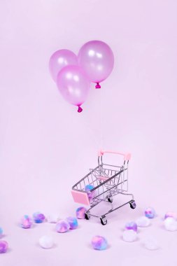 Pastel pembe alışveriş arabası pembe arka plan fotoğrafında balonla yüzüyor.