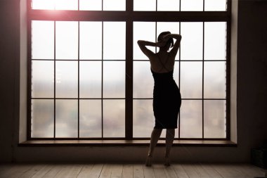 pencereden yakın topuklar üzerinde duran güzel bir kadın silüeti ve saçlarını tutarak