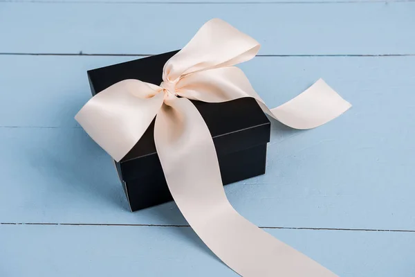 a black box with ribbons of cream-colored on a blue background a gift for women