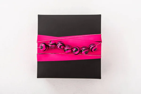 black box with raspberry ribbon and beads with stains on white background