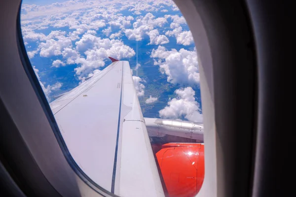 Fenêtre de l'avion en vol : aile, moteur rouge et nuages en arrière-plan — Photo