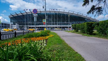 Moskova / Rusya - 18 Haziran 2019: Vnokovo Havaalanı'na çiçeklerle dolu yeşil sokak. Arka planda terminal yakınında taksi ve arabalar.