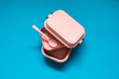Boş pembe bento öğle yemeği kutusu mavi zemin üzerine kaşıkla