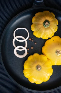 Dilimlenmiş soğan ve karabiber ile siyah bir tavada sarı kabak. Dikey yönlendirme