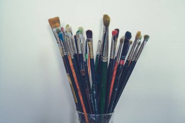 Beyaz duvar arka planda cam birçok boya fırçaları. Yatay yönlendirme