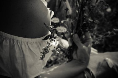 Beyaz bir elbise içinde çıplak bir omuz elinde çayır çiçekleri küçük bir buket. Monokrom. Yatay yönlendirme.