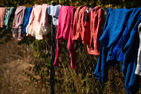 Çok renkli çocuk giysileri güneşli bir günde bir tel çit üzerinde yıkandıktan sonra kuru. Bulanık arka plan. Yatay yönlendirme. Sıcak ton.