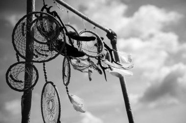 Rüzgarda birçok rüya yakalayıcılar. Kare rafa bağlı. Tüyler ve boncuklarla süslenmiş. Bulutlarla gökyüzünün arka planında. Monokrom. Yatay yönlendirme.