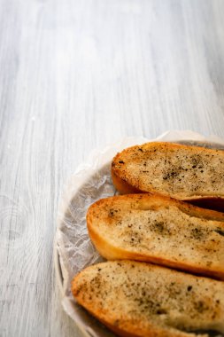 Ön planda, beyaz ahşap bir yüzey üzerinde, buruşuk bir kabartma kağıdının üzerinde gri bir tabakta, karabiberli üç kızarmış ekmek. düşey yönelim.