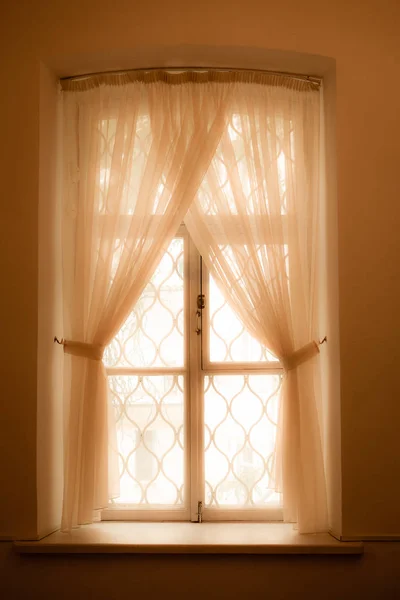 Dantel ızgaralı ve hassas tüllü pencere açık sarı-pembe renktedir. Sıcaklık. Dikey yönelim.