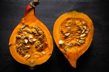 Ortasında tohumlar olan yarı yarıya balkabağı. Karanlık bir tahta yüzeyde. İki yarım. Yatay yönelim.