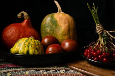 Karanlık bir arka planda balkabağı, domates ve viburnum ile sonbahar sakin bir hayat. Tahtadaki büyük ve küçük sebzeler ve kırmızı böğürtlenler.