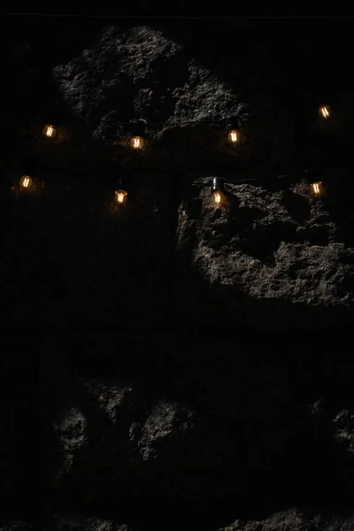 Stone wall background dark with little yellow lanterns in garland. Large relief stone blocks on the wall.