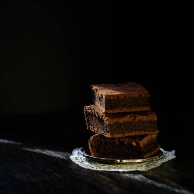 Üç parça browni turtası ve siyah arka planda küçük bir tabak. Çikolatalı tatlı..