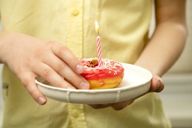 Bir çocuğun eli tabaktan bir donut aldı. Sarı tişörtlü bir gencin ellerinde tatil pastası
