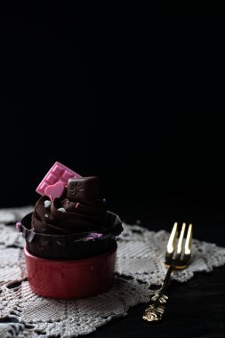 Eski bir peçetenin üzerinde pembe küçük çikolatalı kek ve arka planda yaldızlı çatal. Mutlu Yıllar ya da Sevgililer Günü için klasik tebrik kartı.