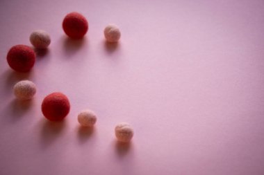 Büyük, koyu ve küçük, hafif yün topları pürüzsüz pembe bir yüzey üzerinde yarım kalp şeklindedir. İğneyle kurumuş hisler..