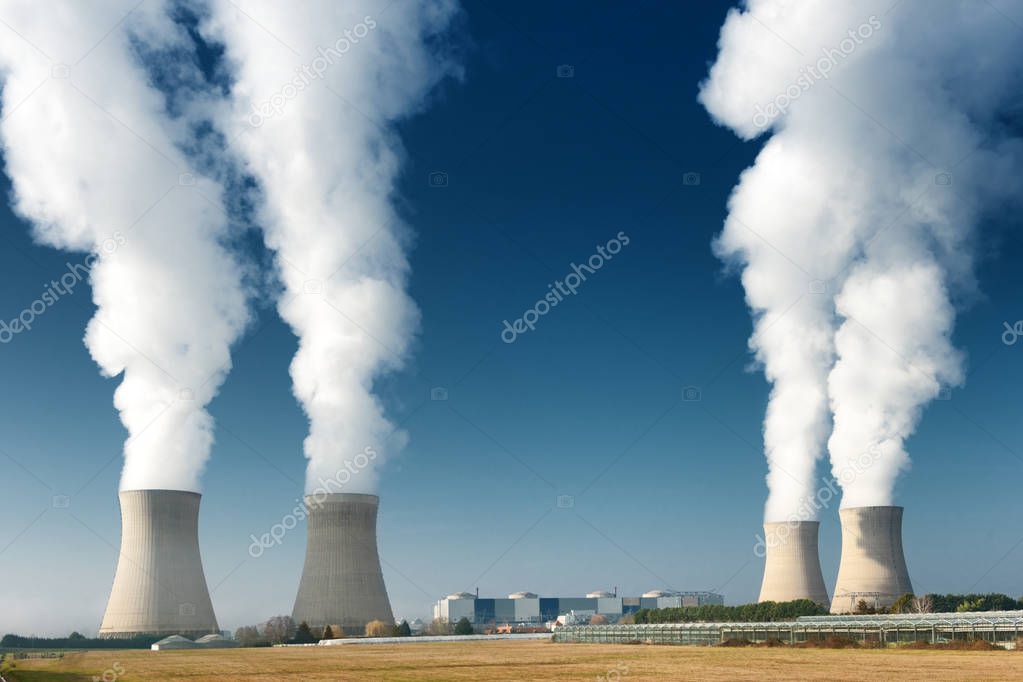 four power plant cooling towers steaming on dark blue sky background