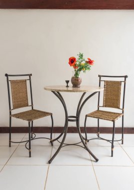 Dikey boş kır sandalyeleri ve çiçeklerle süslenmiş pencerelerden gelen sıcak gün ışığıyla süslenmiş bir masa. Tatil köyü, otel ve rahatlama kavramları