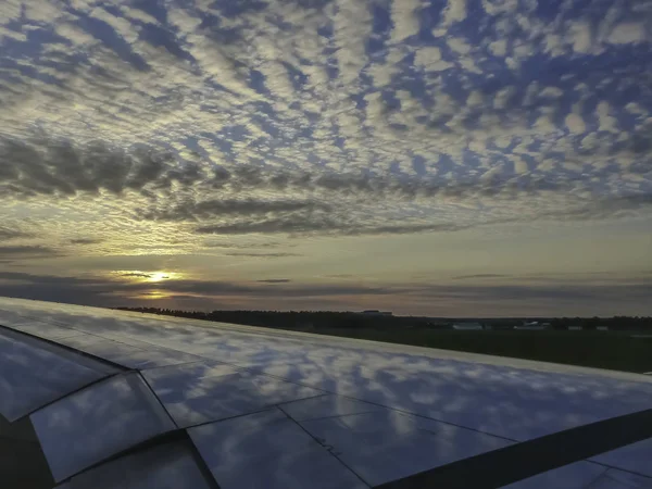 Wolken und blauer Himmel, die sich bei Sonnenuntergang auf dem Flugzeugflügel spiegeln. — Stockfoto