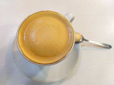 Beyaz fincan kahve süt beyaz bir tablo üzerinde beyaz bir daire üzerinde metalik bir çay kaşığı ile