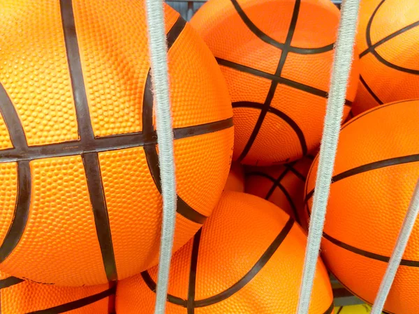 Grupo de muchas bolas nuevas de baloncesto naranja con líneas negras en una tienda de deporte listo para ser vendido detrás de algunas cuerdas blancas elásticas — Foto de Stock