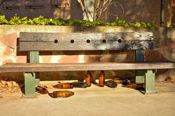 много больших оранжевых бутылок пива из стекла полностью пустым в парке из-за того, что кто-то выпил время, прежде чем оставить их под коричневой скамейкой в солнечный день
