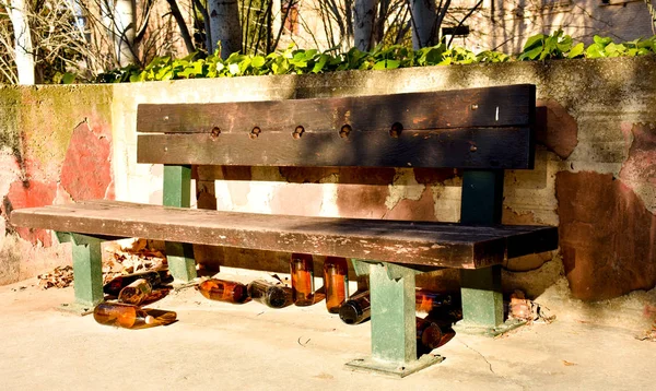Many big orange bottles of beer made of glass completely empty at the park due to somebody has drunk time before leaving them under a brown bench in a sunny day — Stock Photo, Image