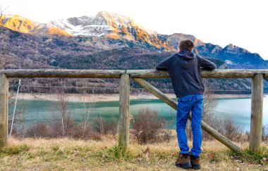 Çocuk kollarını öğleden sonra kar dağların doruklarına ve masmavi bir deniz göl üzerinde gözlemleyerek ahşap bir çit ile.