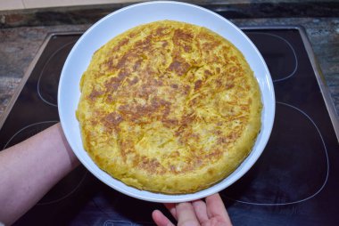 lezzetli İspanyol omleti bir indüksiyon Ocak ve fırın mutfak, beyaz tabakta lezzetli omlet gösterilen siyah bir tavada pişmiş yumurta, patates, soğan ile