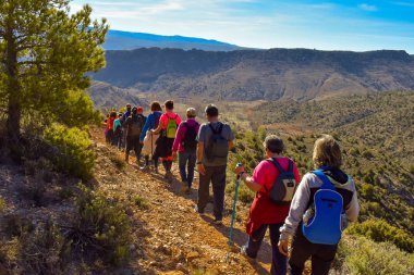Grup kum ve taşların bir dağ inanılmaz bir manzara ile arka planda yürüyen muhteşem güneşli bir günde yola trekking renkli sırt çantası ile yetişkin insan.